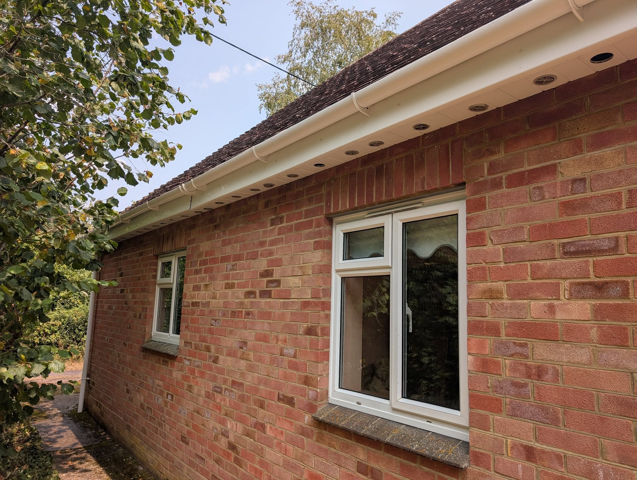 The side of a red-brick bungalow with clean windows and white fascia
