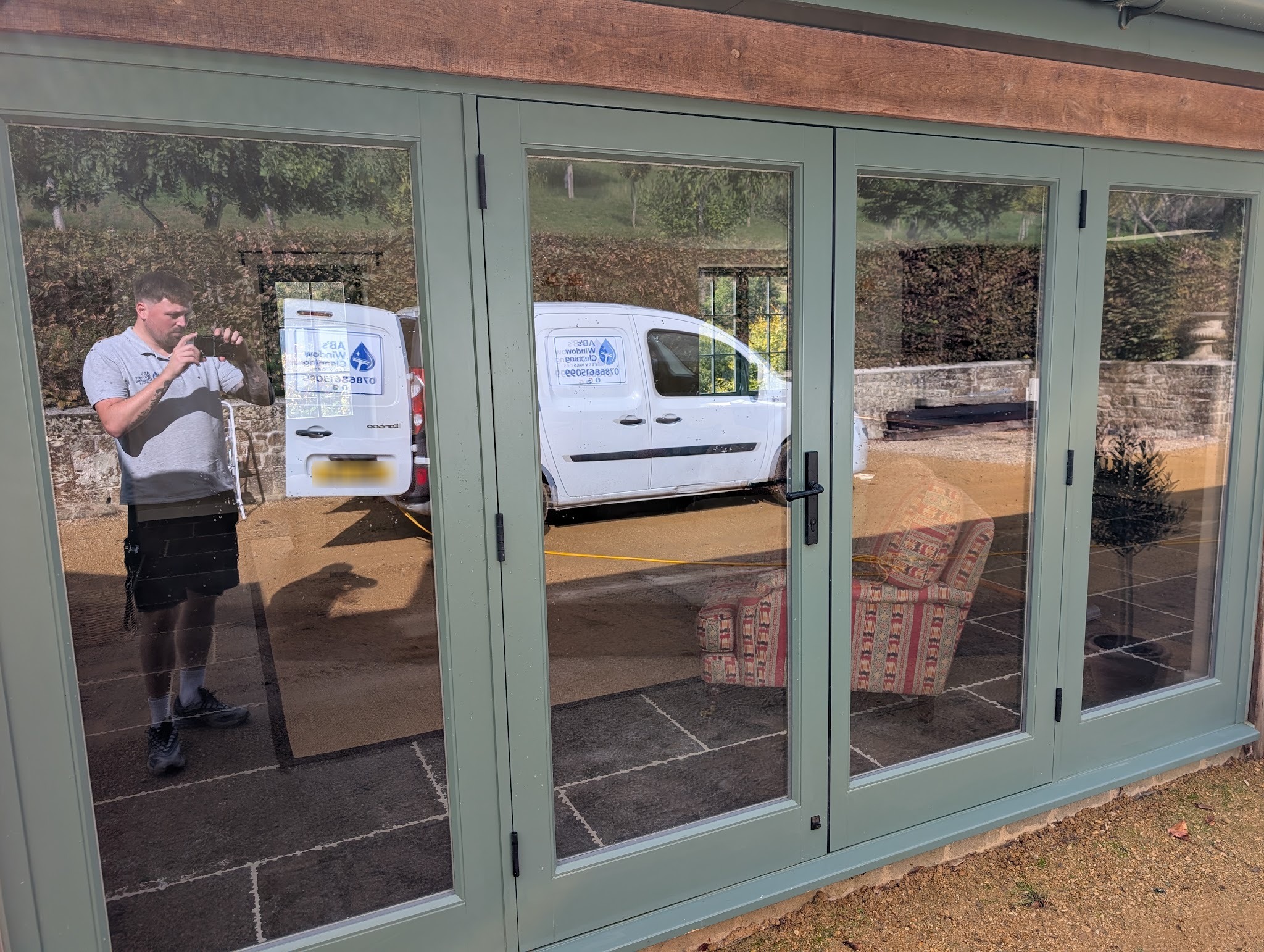 Freshly cleaned sage green bifold doors reflecting the AB's Window Cleaning van